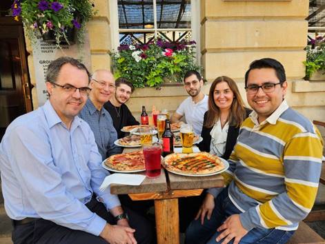 A group of people sitting at a table with pizzas and drinks

Description automatically generated